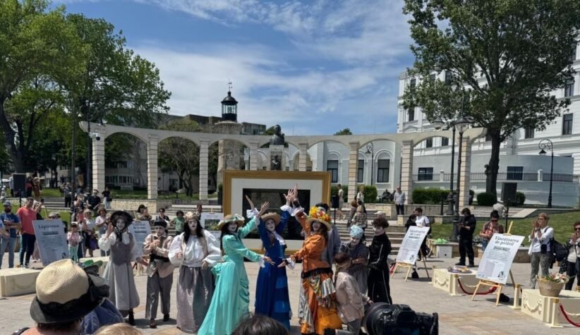 Group of performers in vintage costumes posing and dancing in a sunny outdoor plaza; audience watches in the background.
