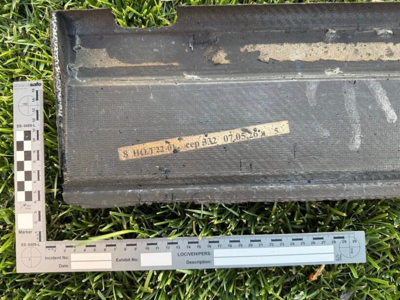 Black rectangular case on grass with a beige labeled tape and two measurement rulers nearby, suggesting field evidence tagging.