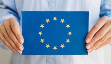 Person holding a blue card displaying the European Union flag: circle of 12 gold stars around a center space.