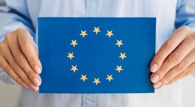 Person holding a blue card displaying the European Union flag: circle of 12 gold stars around a center space.