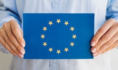 Person holding a blue card displaying the European Union flag: circle of 12 gold stars around a center space.