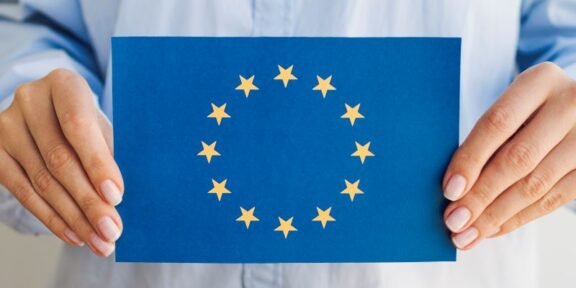 Person holding a blue card displaying the European Union flag: circle of 12 gold stars around a center space.