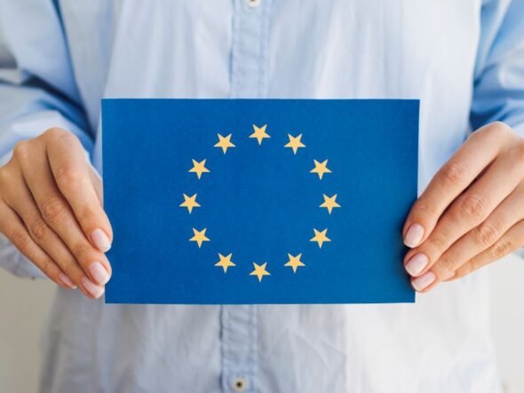 Person holding a blue card displaying the European Union flag: circle of 12 gold stars around a center space.