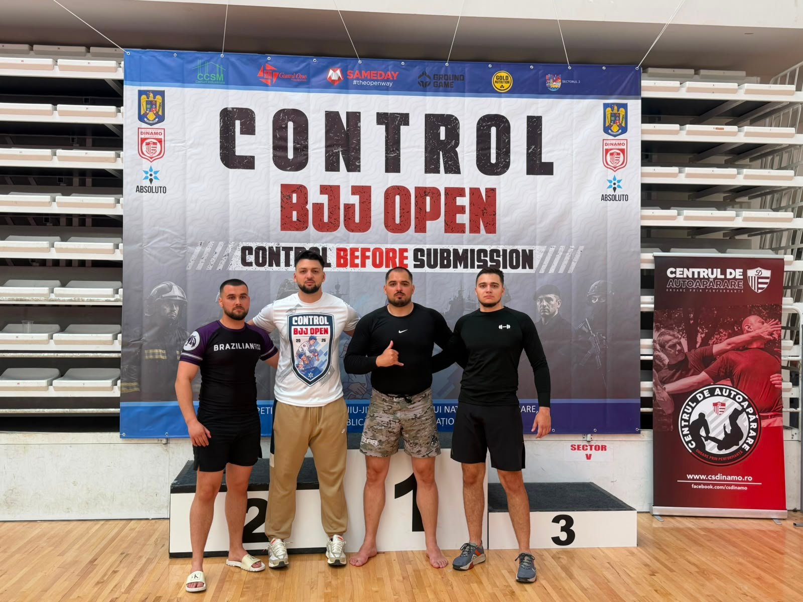 Four men stand on a winners podium in front of a banner that reads 'CONTROL BJJ OPEN', posing for a photo at a martial arts event.
