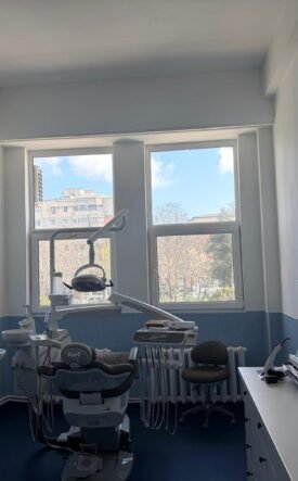 Dental treatment room with a patient chair, overhead light, and dental tools ready for a procedure near large windows.