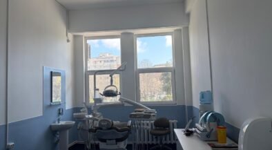 Dental treatment room with a patient chair, overhead light, and dental tools ready for a procedure near large windows.