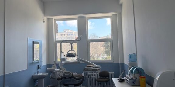 Dental treatment room with a patient chair, overhead light, and dental tools ready for a procedure near large windows.