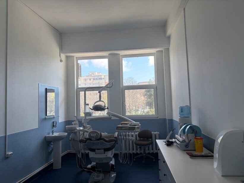 Dental treatment room with a patient chair, overhead light, and dental tools ready for a procedure near large windows.