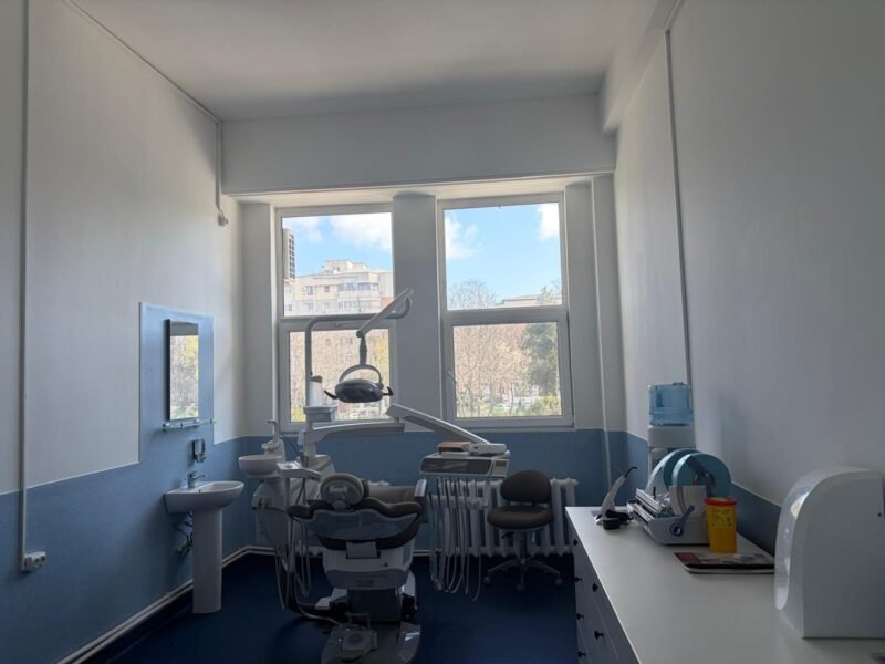 Dental treatment room with a patient chair, overhead light, and dental tools ready for a procedure near large windows.