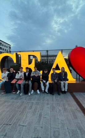 Group of people sitting on a low wall in front of large, illuminated letters spelling 'SUCEAVA' with a red heart graphic between letters.