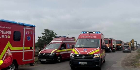 Convoy of red emergency vehicles, including SMURD ambulances, parked on a road under a cloudy sky