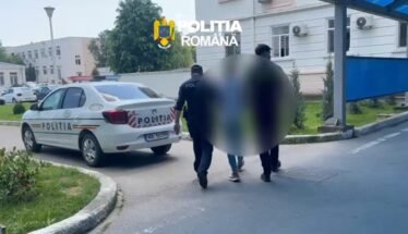 Romanian police car parked outside a building as officers escort two blurred individuals into the entrance.